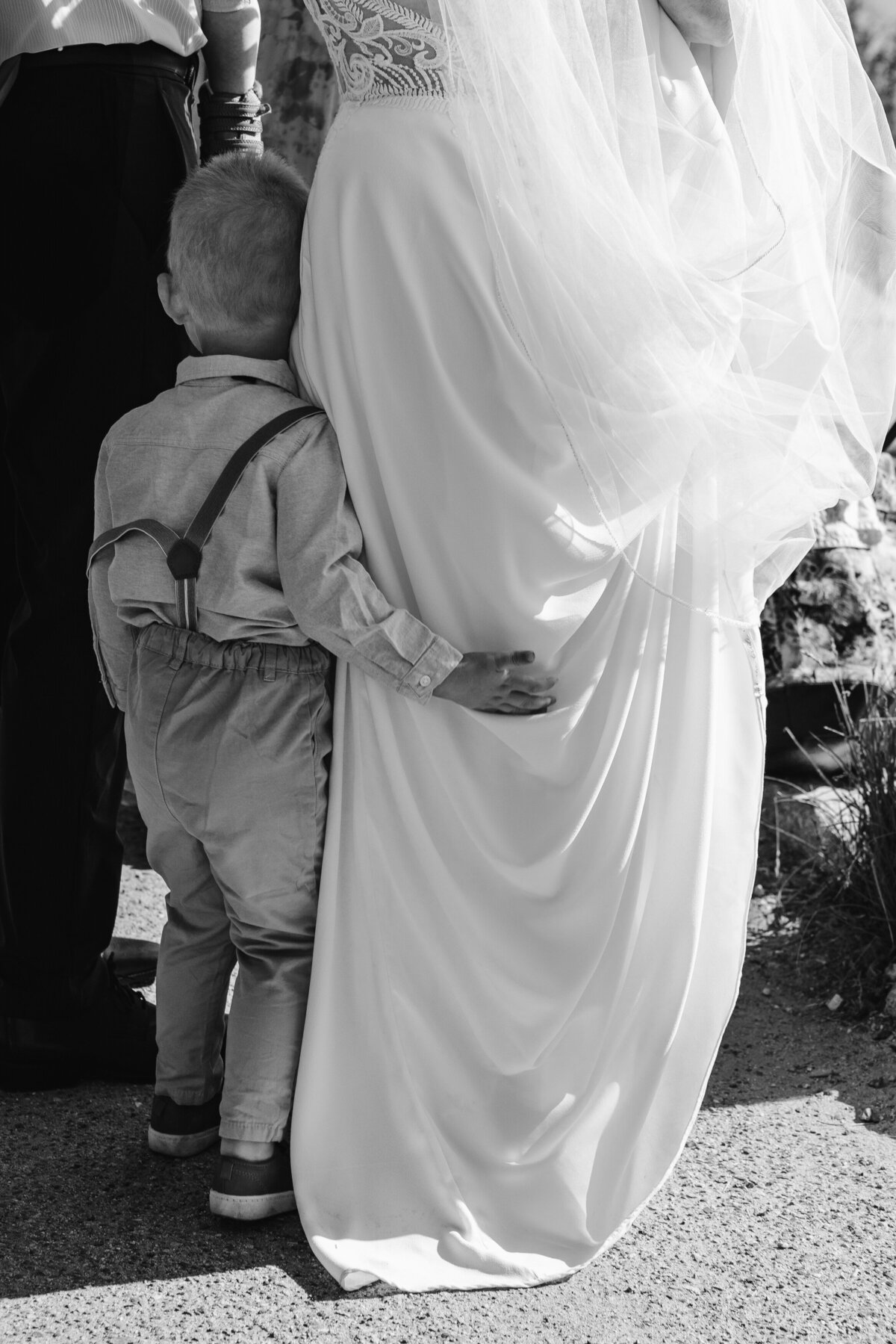 A small child with their arm around the legs of someone in a wedding dress