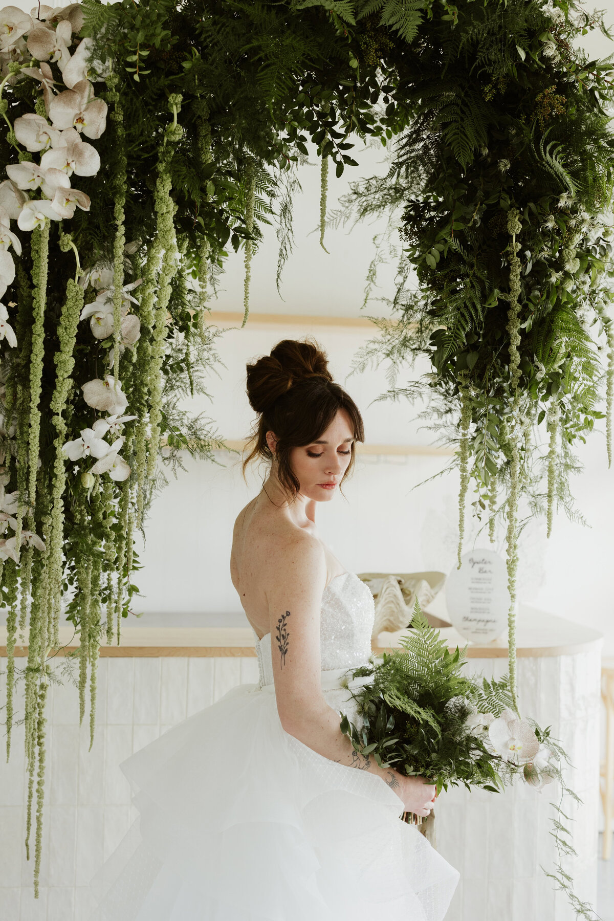 Bride beautiful in white under the floral wedding arch while holding her leaf bouquet