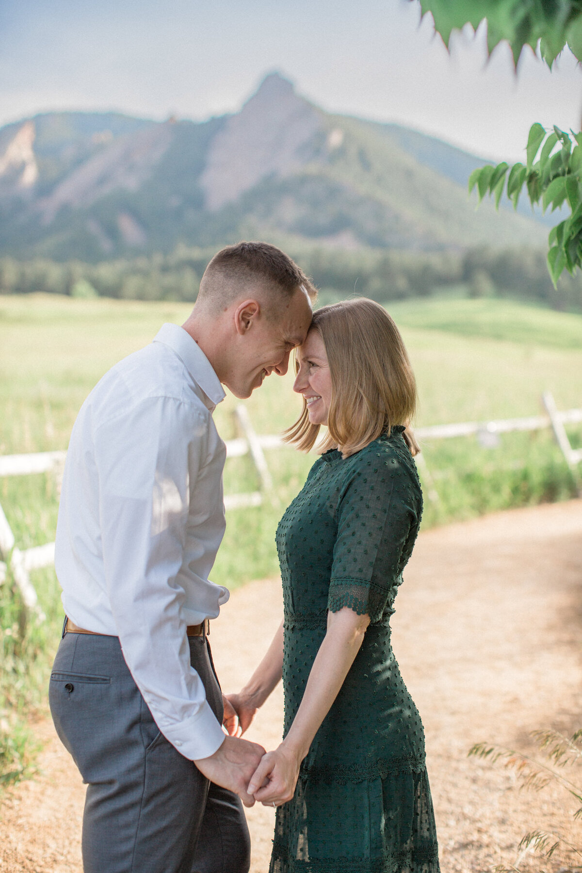 A couple, hand in hand, touch their foreheads together during their engagement session at Chautauqua park