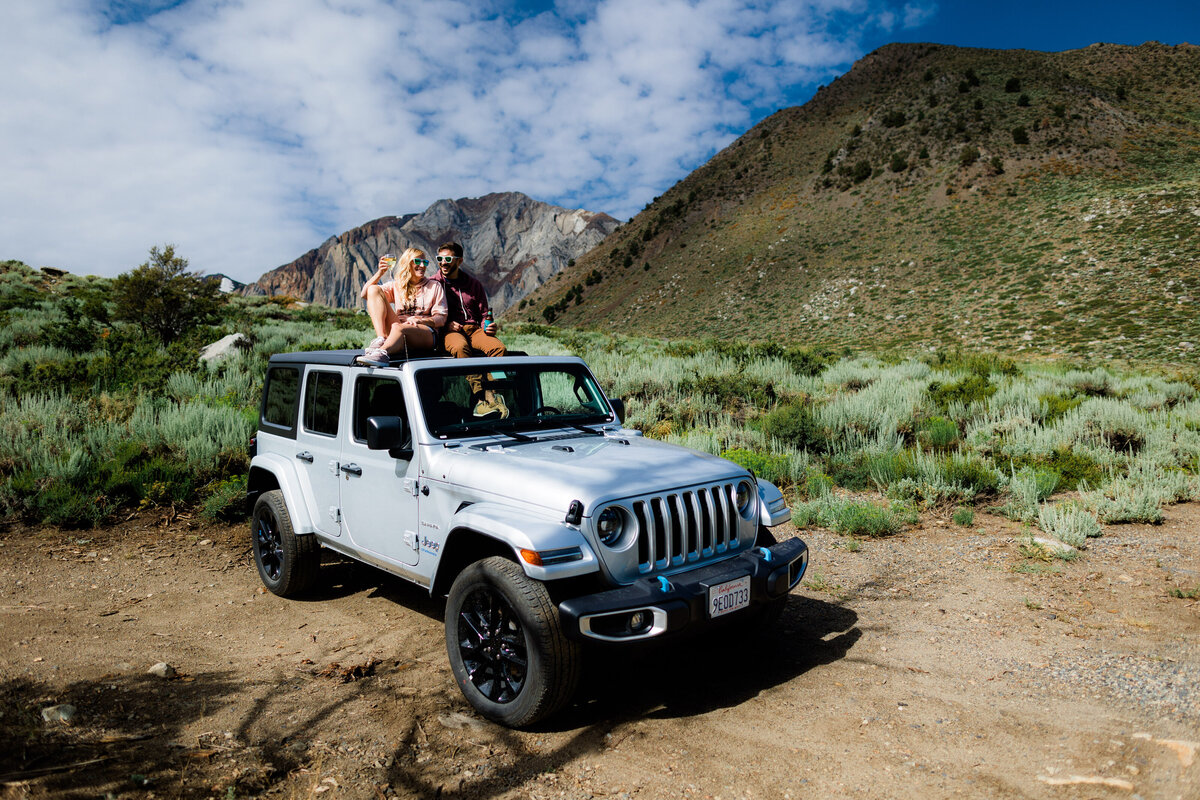 A couple sitting on top of a jeep smiling