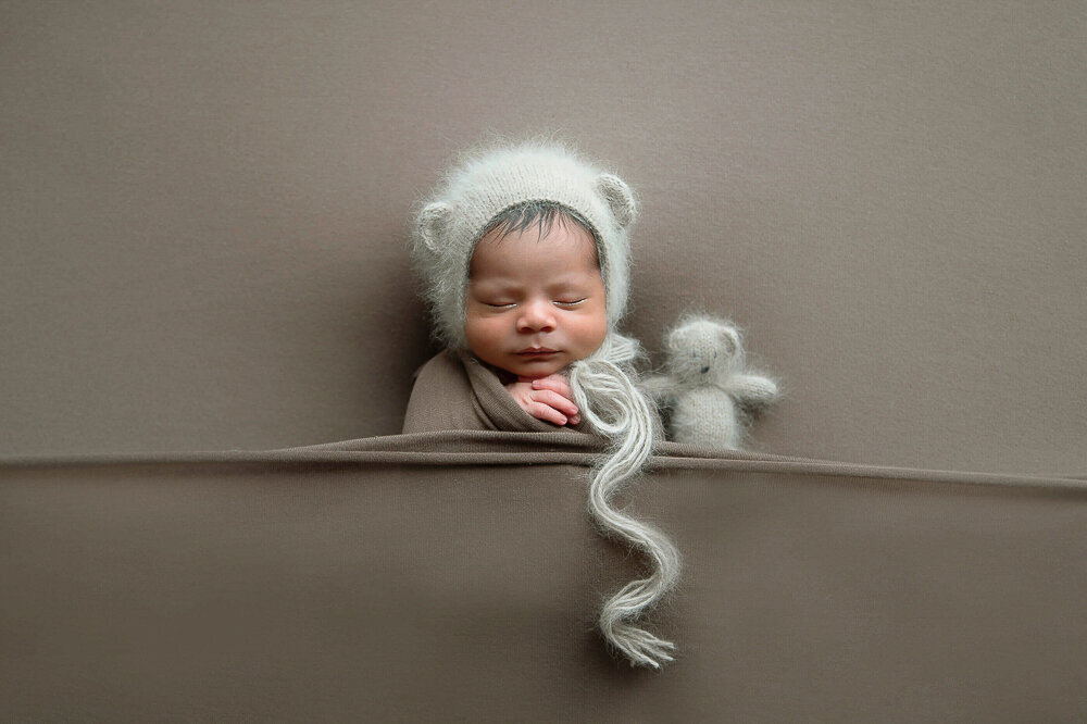 newborn baby boy with a bear hat and a bear for his newborn photography session in Hamilton, Ontario.