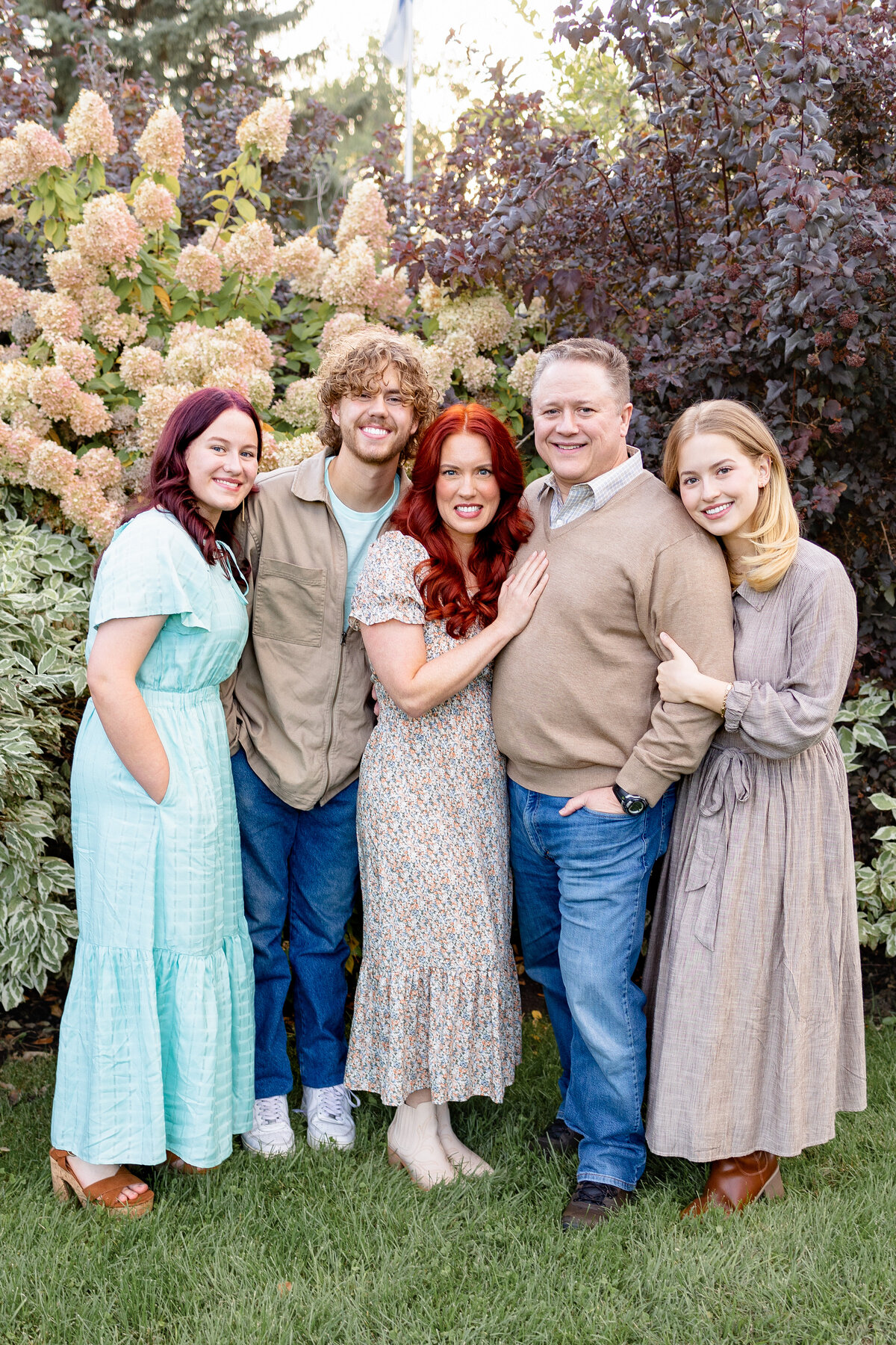 A close-knit family poses together in front of lush greenery and blooming flowers, capturing their bond in a natural setting.