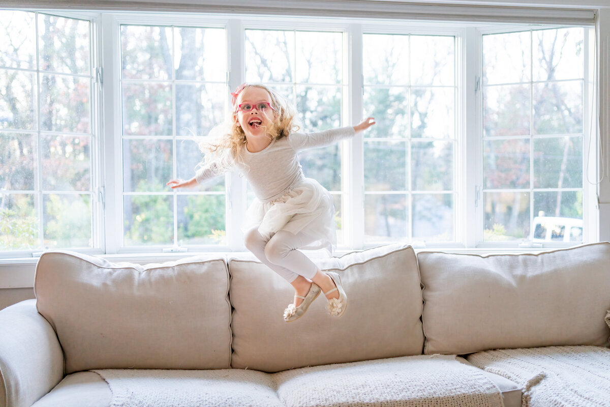 Little girl jumps on couch during her family's in home family session in Wayland MA