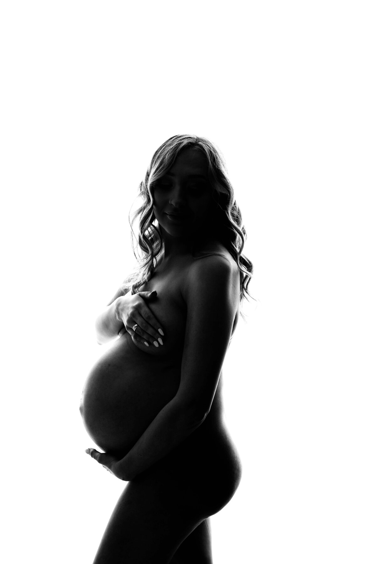 A very modern, nude maternity photo captured perfectly by Mobile, AL Maternity Photographer. The mom is backlight, and the image is black and white. The shadowy editing perfectly highlights the details of moms growing baby bump, while providing modesty.
