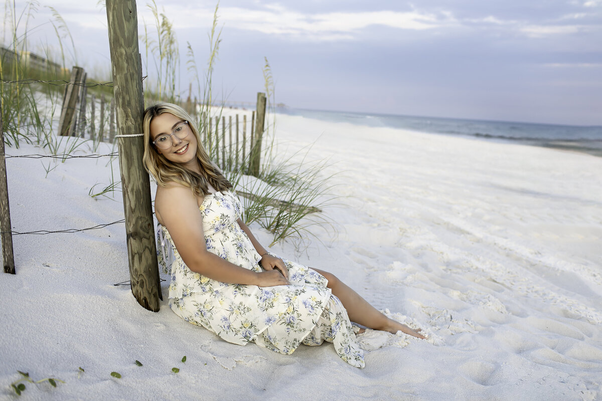 A high school senior enjoying the beach breeze, with the sun setting behind them, capturing the beauty of both the ocean and the excitement of graduation