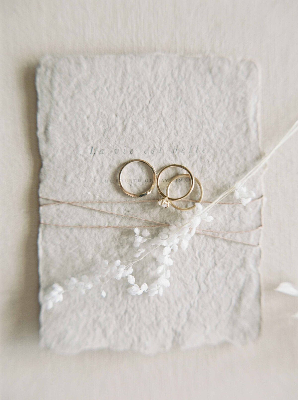 three gold wedding rings laying on textured stationary with white flower sprigs