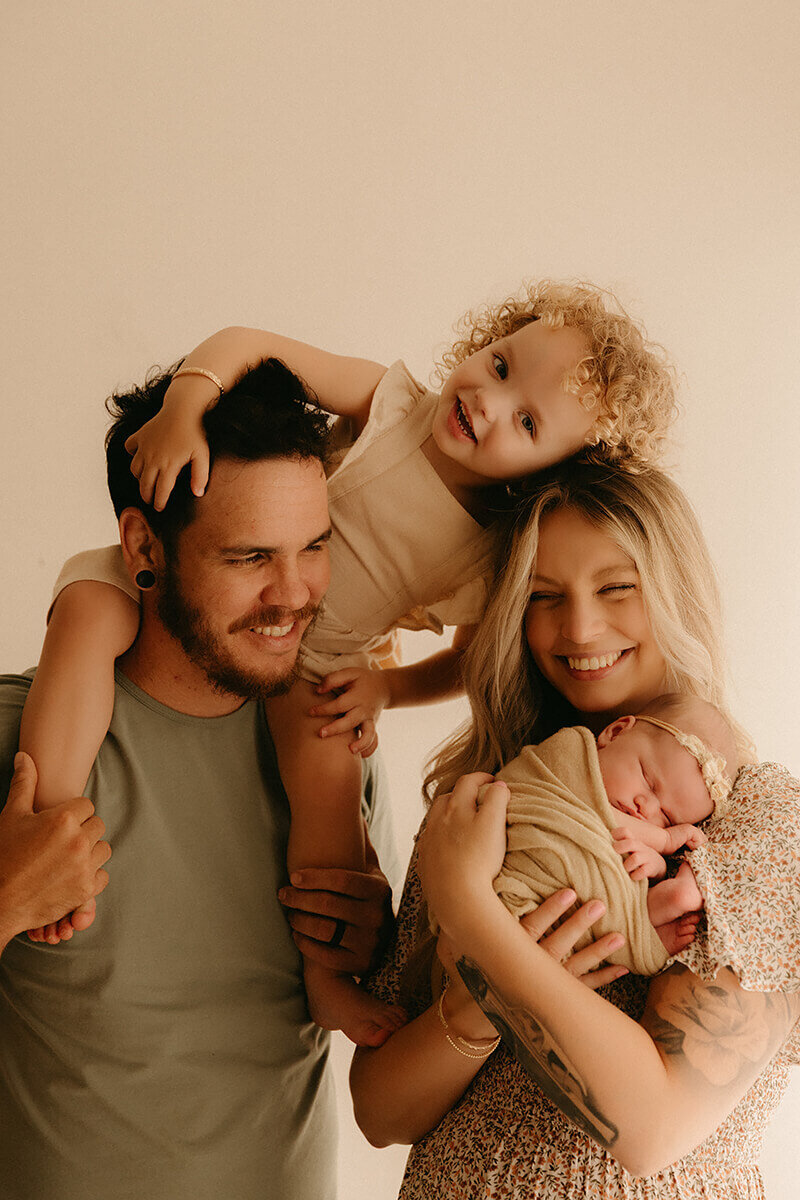 Smiling parents holding newborn and toddler in Nashville photography studio