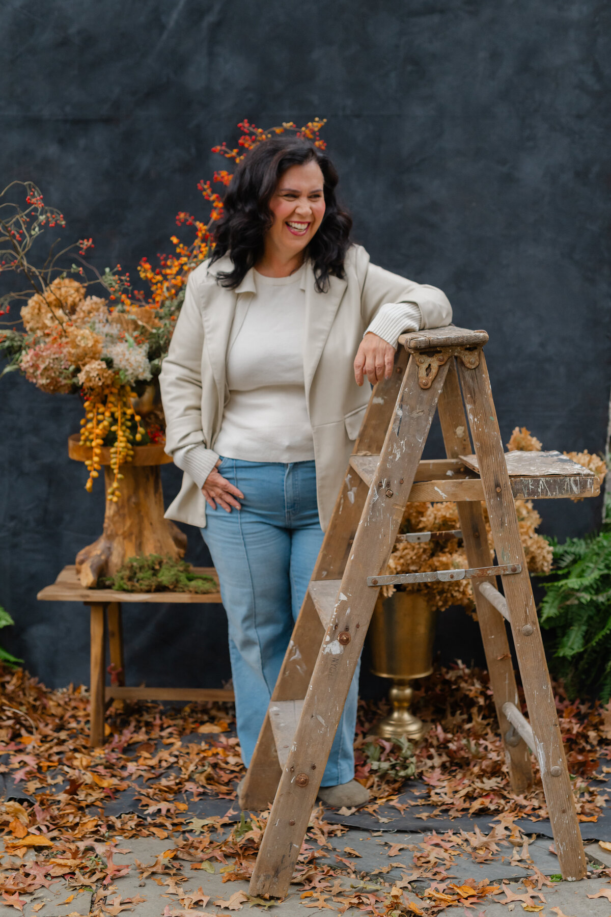 Woman leaning against ladder with fall leaves on ground