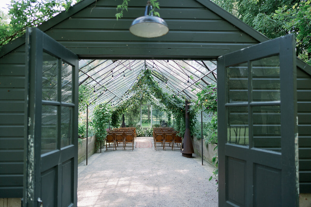 Open greenhouse doors leading to the candlelit dinner setup at Glasshouse Community during an intimate Michigan wedding celebration.
