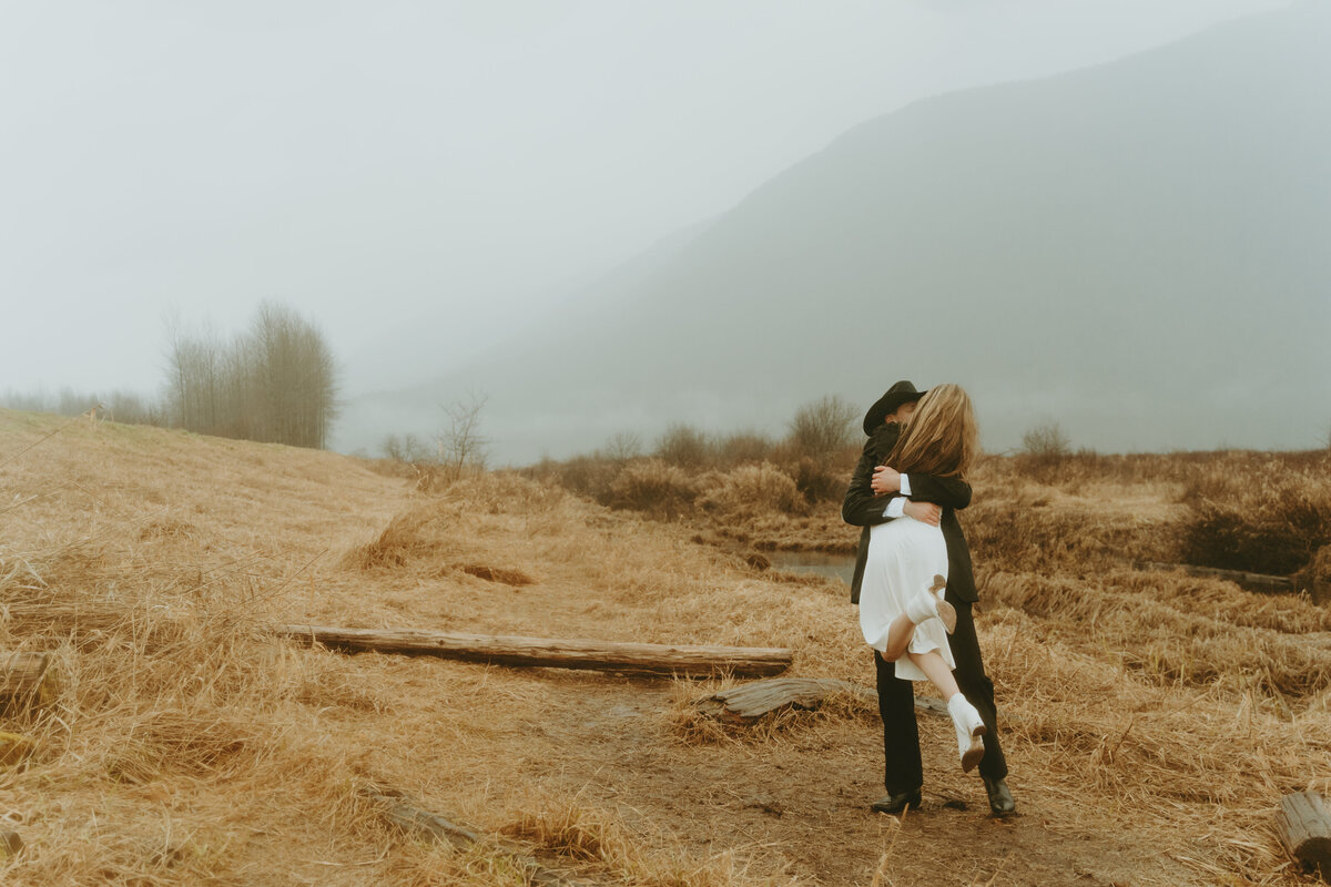 Modern Vivid and Romantic Engagement Landscape Photo in the rain with foggy mountains in the back