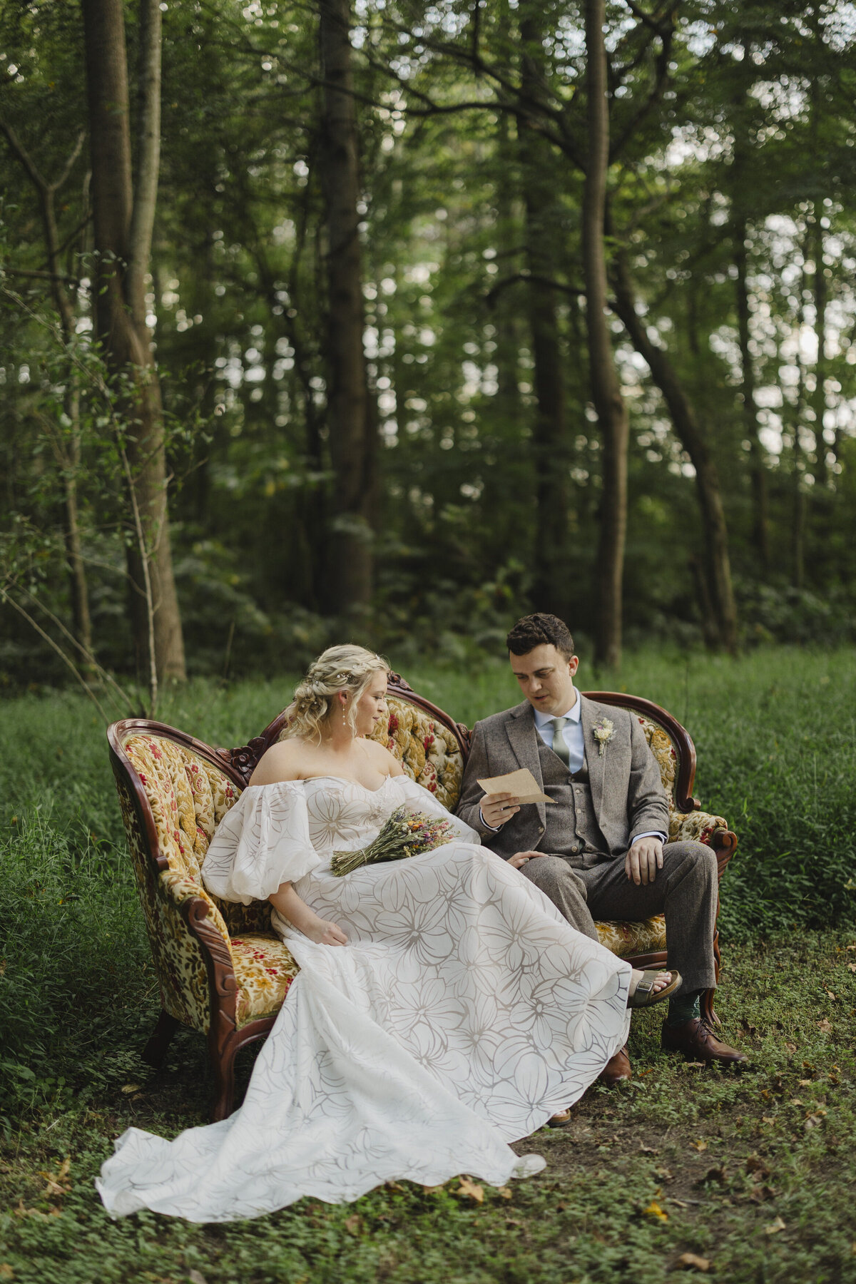 A newlywed couple sitting on a couch together in a field 