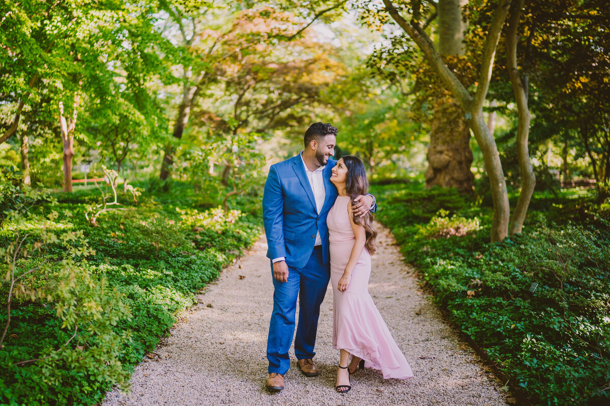 A couple embracing and walking through a walkway at the planting fields arboretum during their engagement session