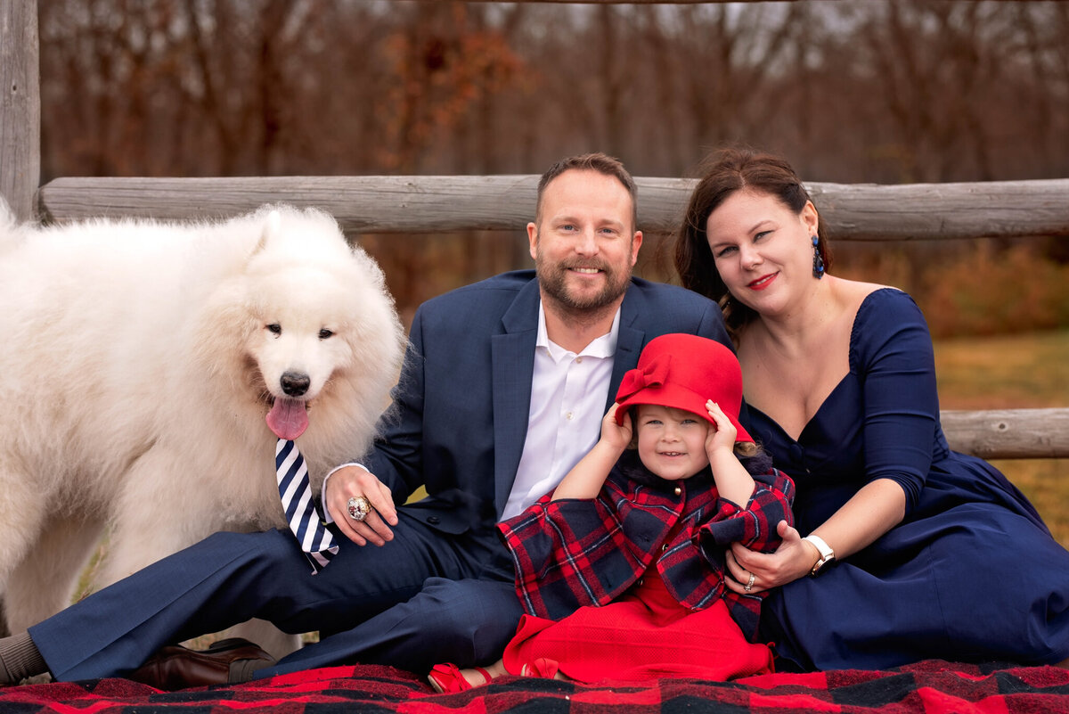 Cozy outdoor winter family portrait featuring parents, children, and their fluffy white dog on a blanket, captured in Lenexa, Kansas. Ideal for pet-friendly family photography with a seasonal touch