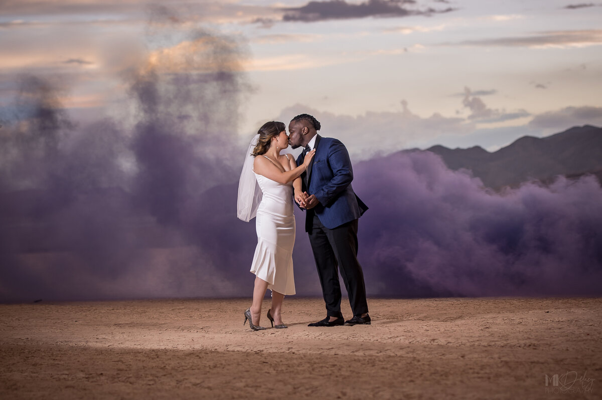 Purple smoke bomb bride in simple white dress groom wearing blue dress jacket kissing on a dry lake bed  in las vegas nevada