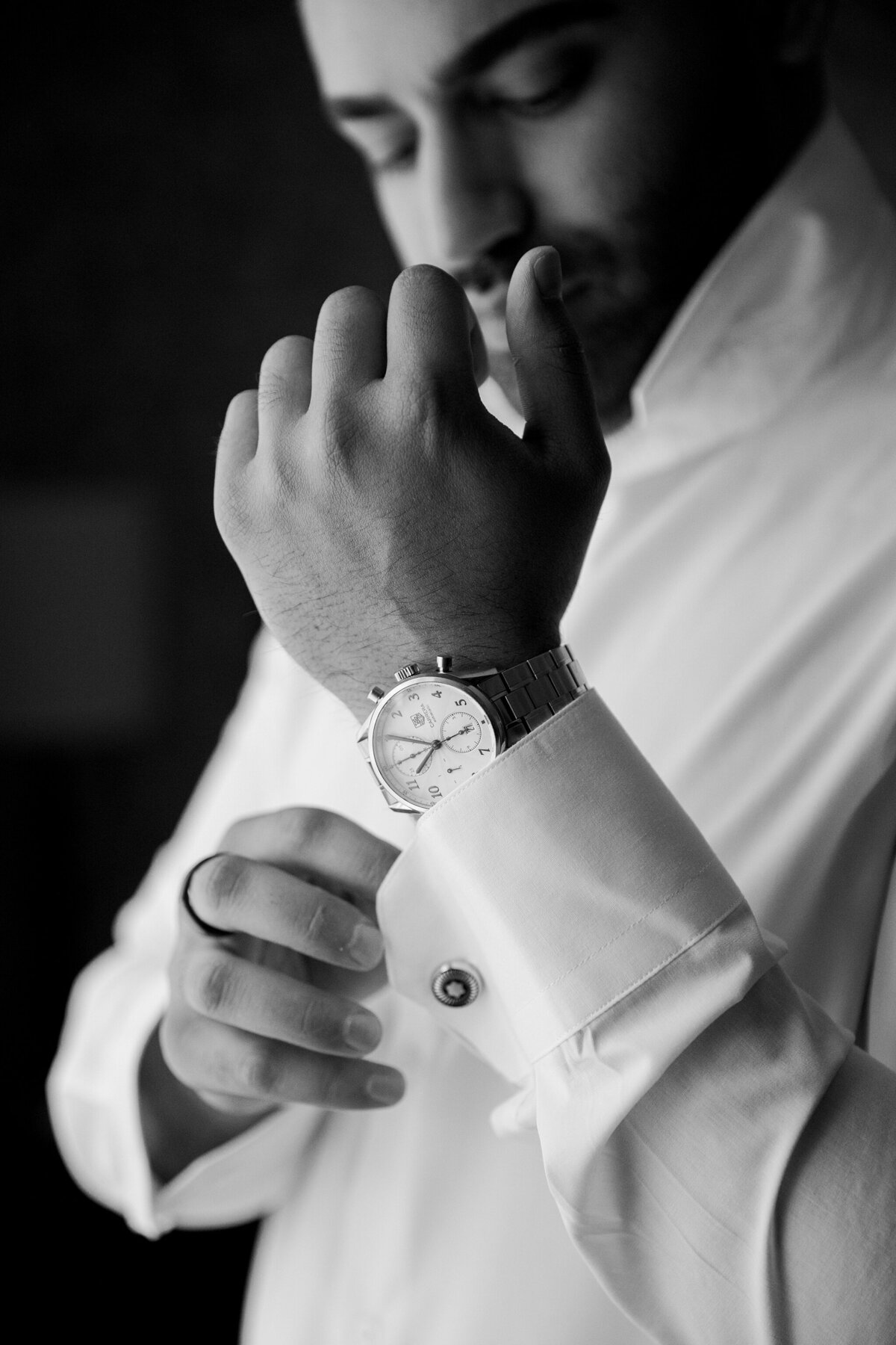 Black and white portrait of a groom adjusting his cufflink and showing off his watch on his wedding day in Dallas, Texas.