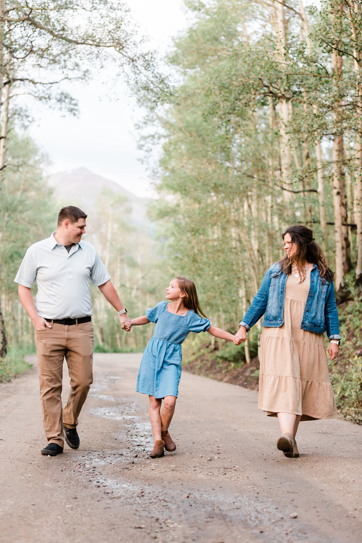 A family of three walk hand in hand through a tunnel of aspen trees
