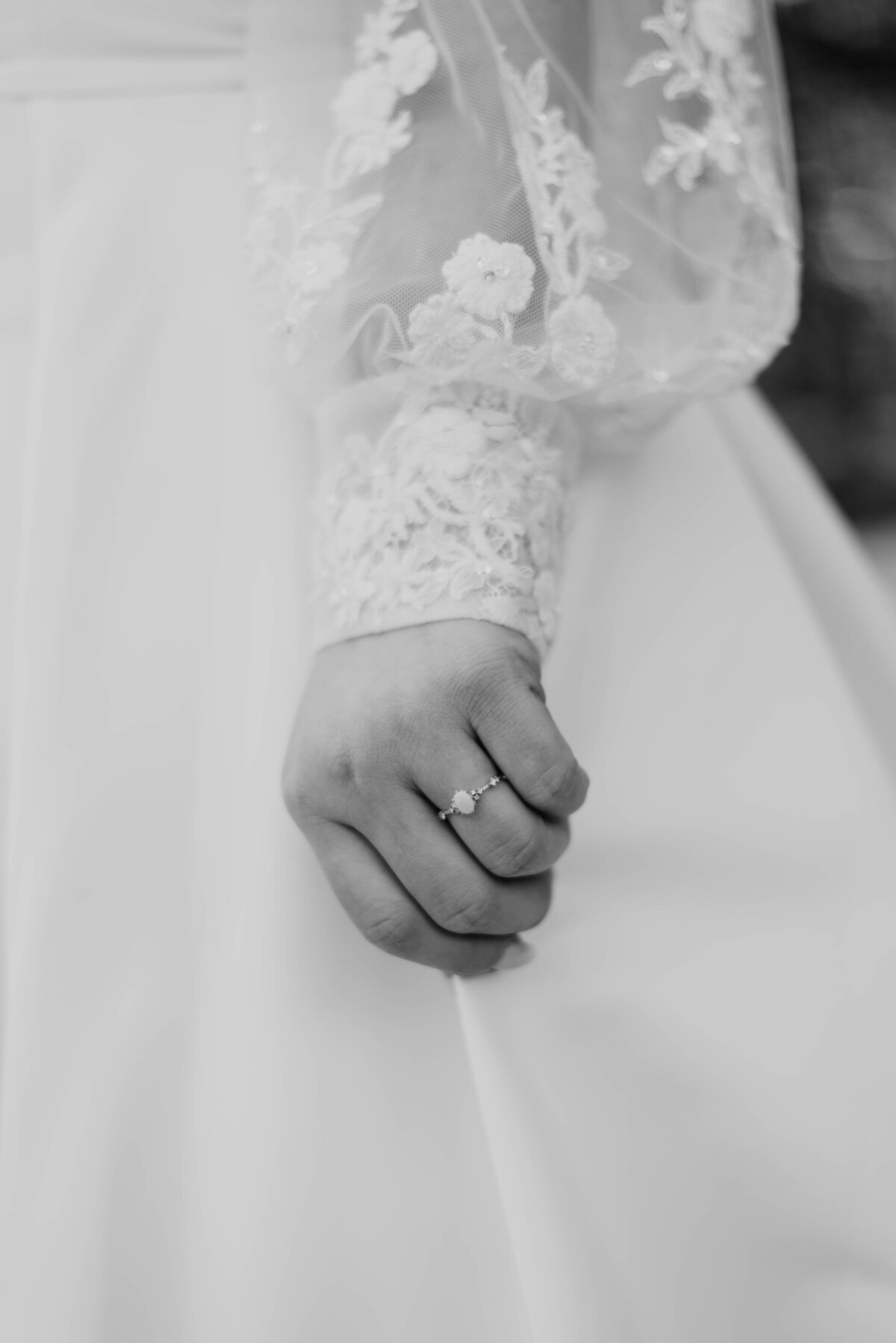 a black and white photo of a brides lace cuffed wedding dress sleeve and her engagement ring.