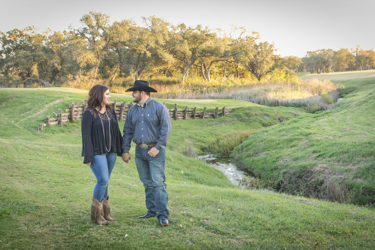 sunset engagement portrait with cowboy hat and ranch fence rolling hills in Texas