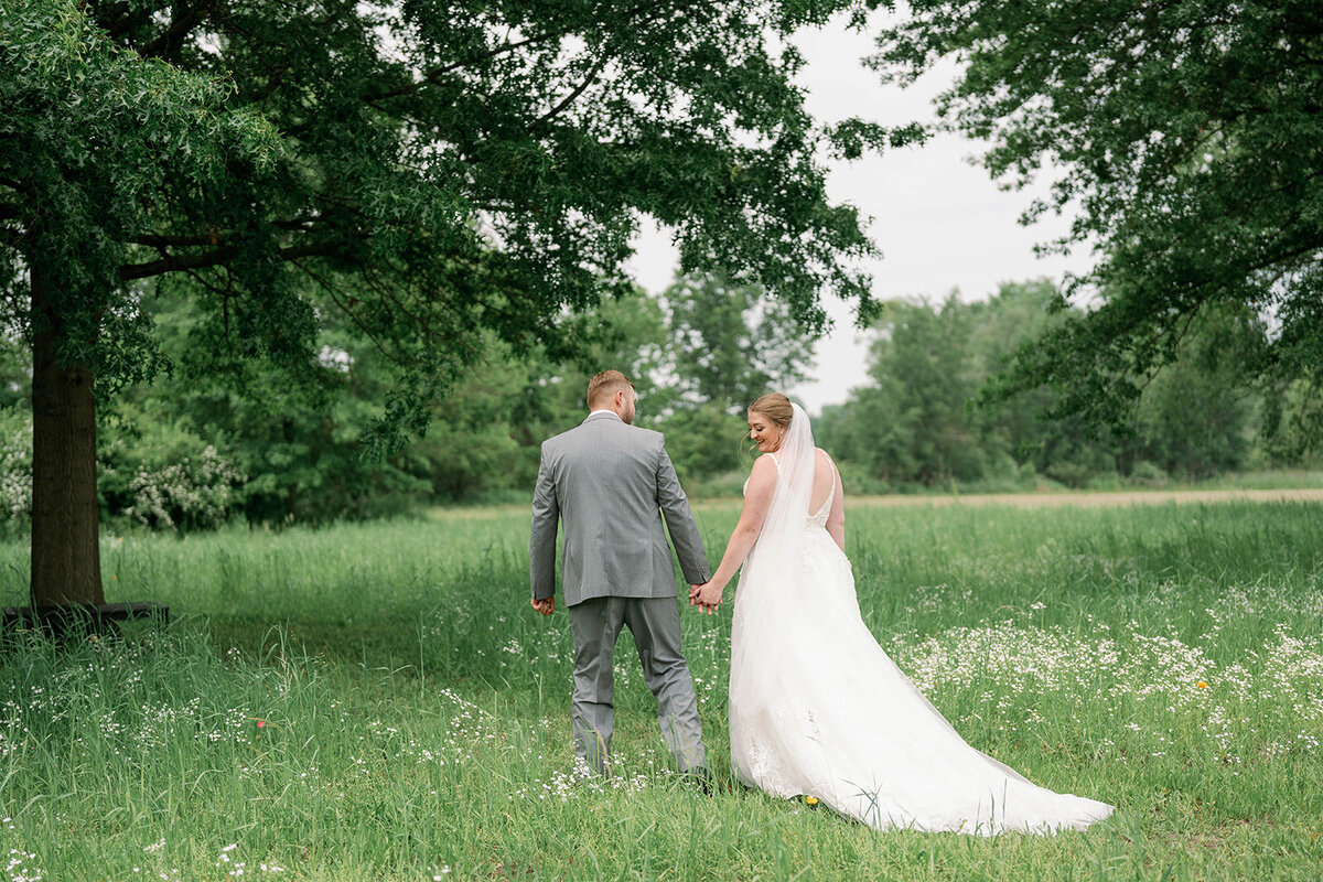 Bride and groom walking hand in hand through a floral field during their Blue Heron Barn wedding portraits in Kalamazoo, Michigan.