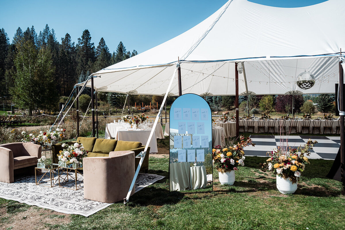 A tent at a wedding reception with a table seating chart and a lounge area.