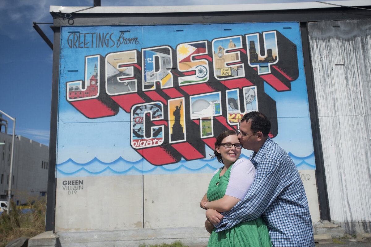 A person hugging their partner from behind as they stand in front of a mural 