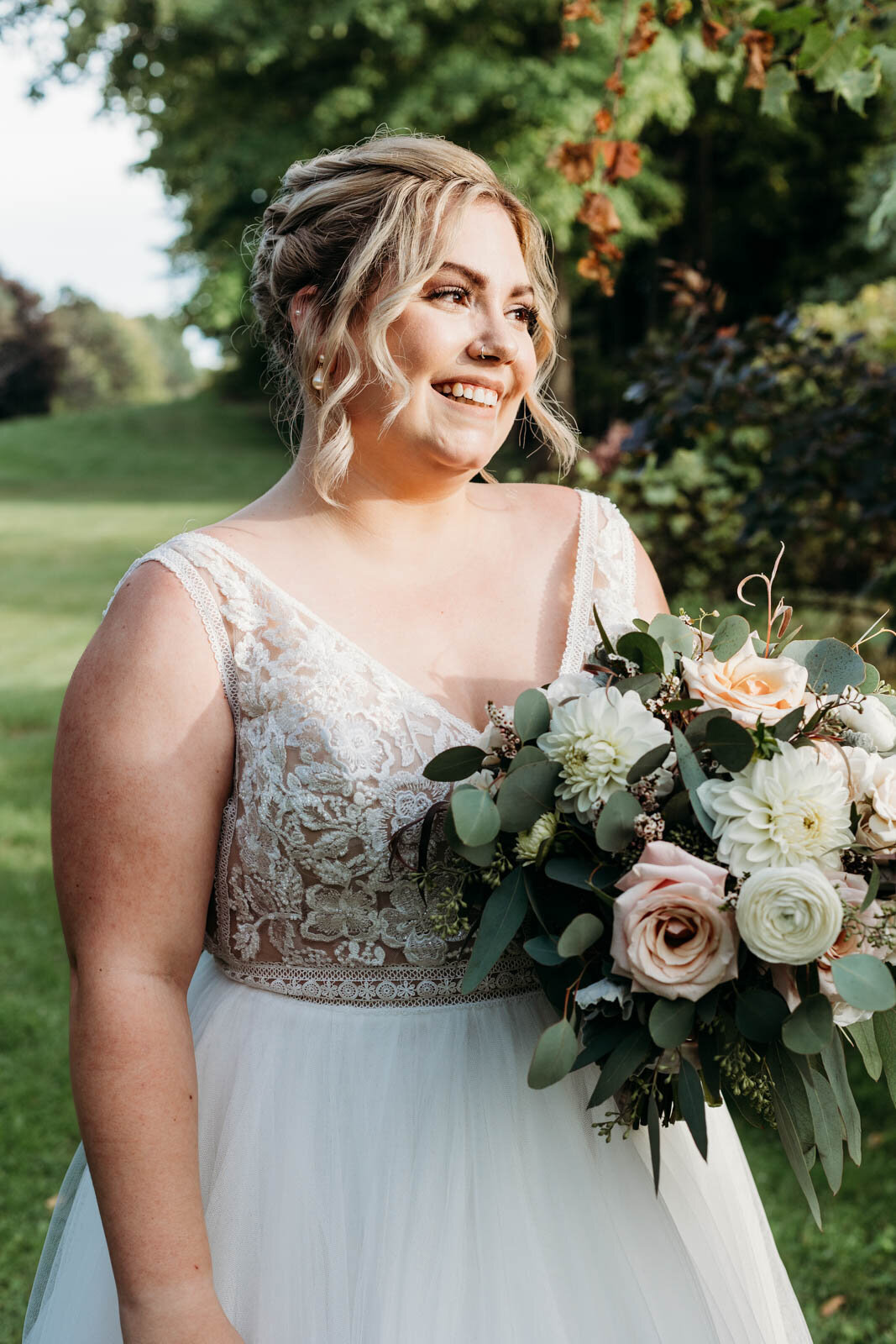 A smiling bride walks in a lawn holding her large white and pink bouquet