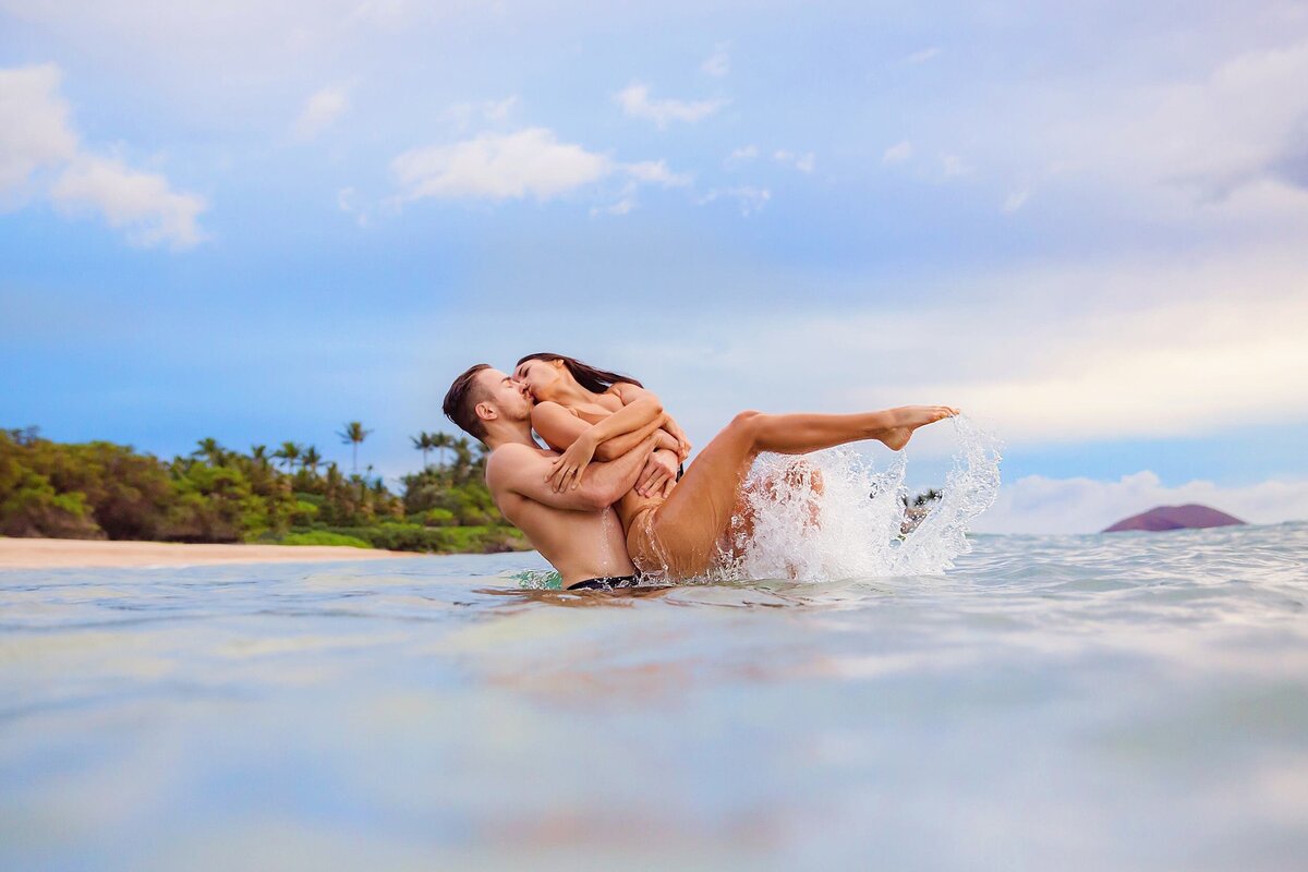 Candid couples water portraits captured at sunrise, woman and man kiss in the ocean and woman lifts her leg, splashing the photographer