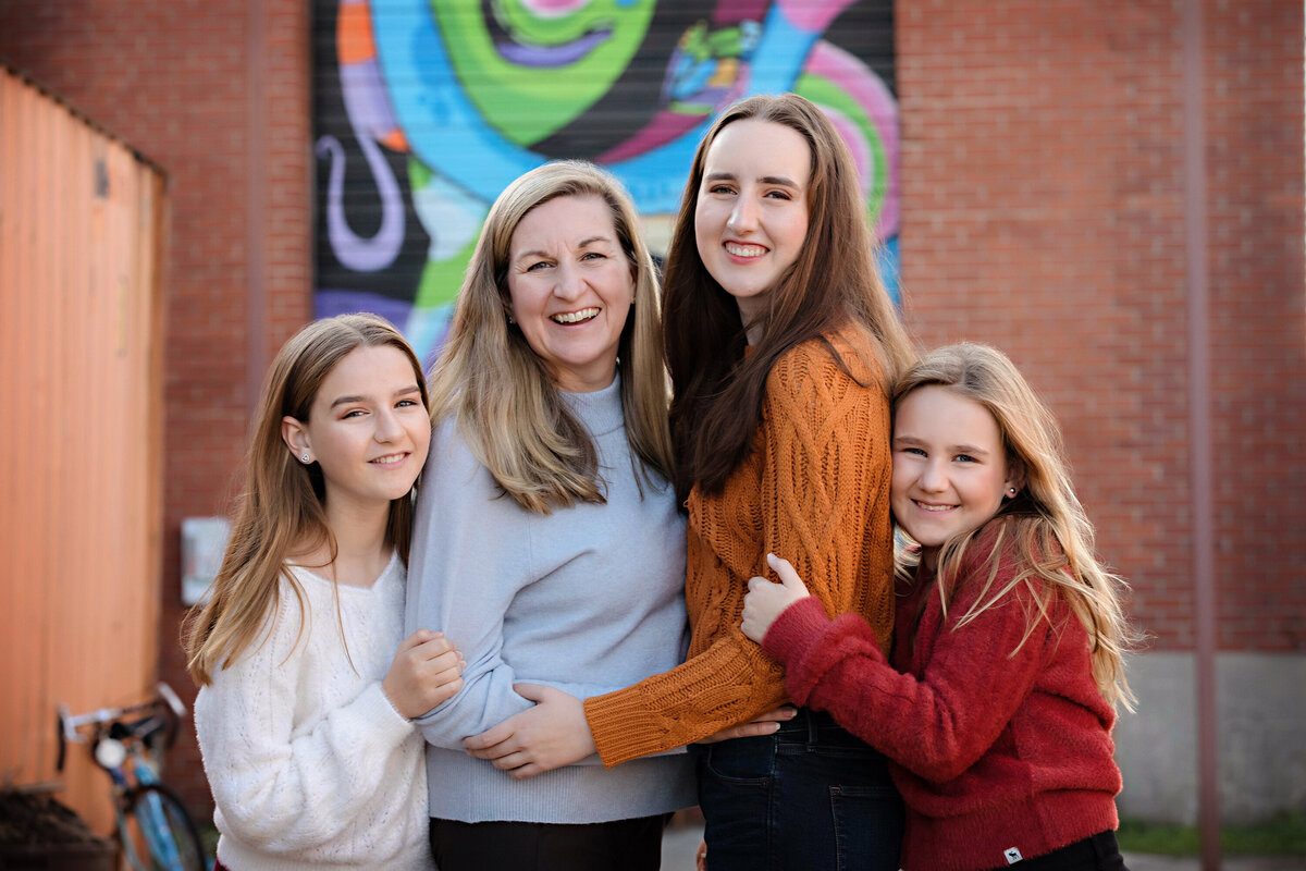 Warm family moment with mom embracing her three girls against a bright, multicolored mural at Camp North End Charlotte NC