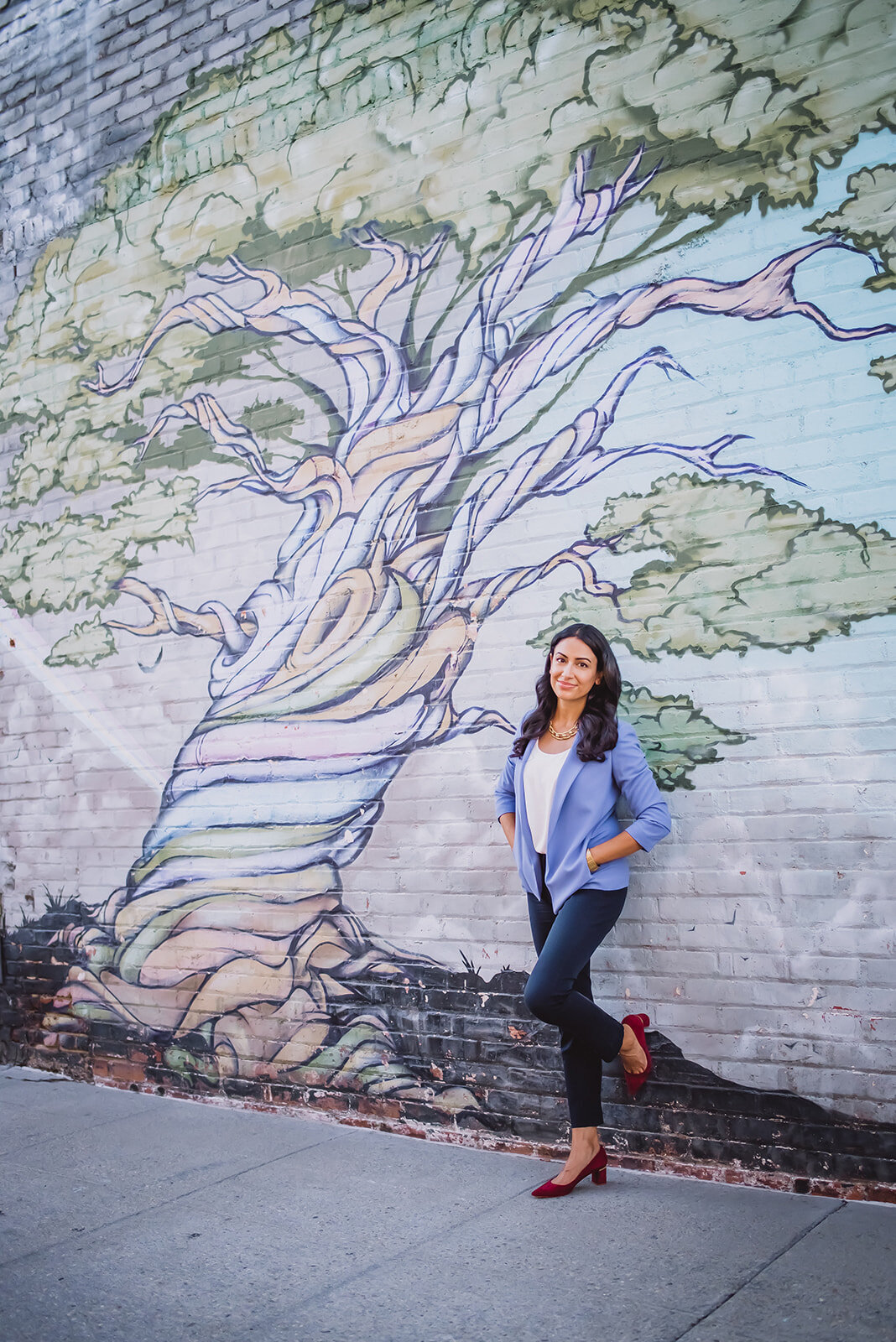 A woman in a blue blazer stands in front of a mural of a tree.