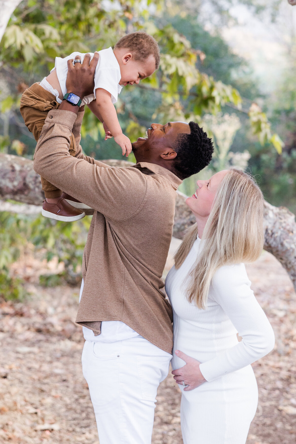 parents holding up toddler son under tree san diego