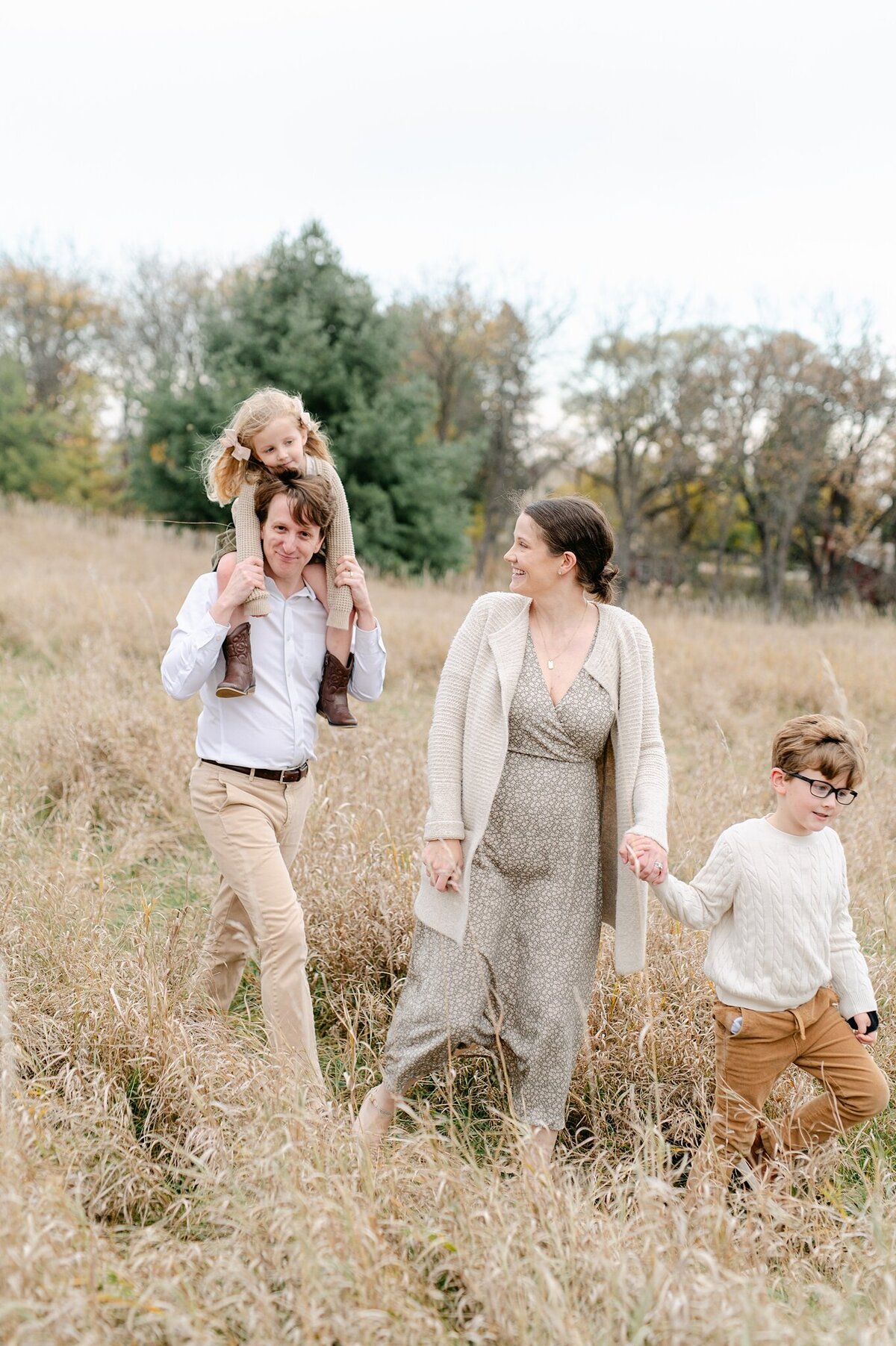 Family of four walking through the field with daughter on her dad's shoulders