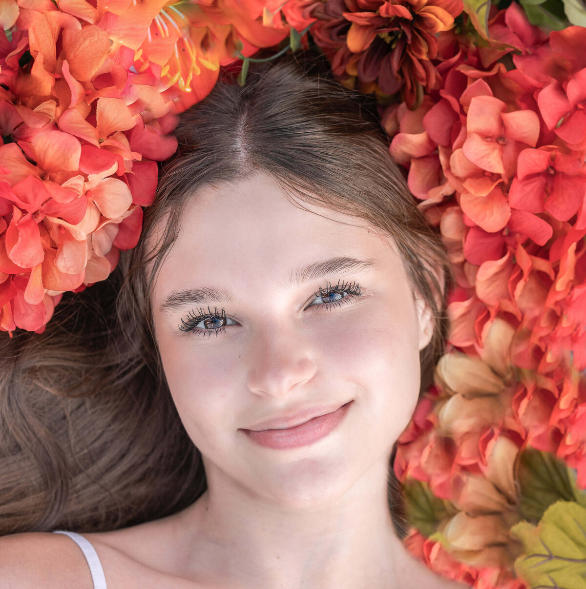 high school girl  laying on a bed of orange flowers looking at the camera by Elizabeth Klusmann, an Atlanta Senior  photographer