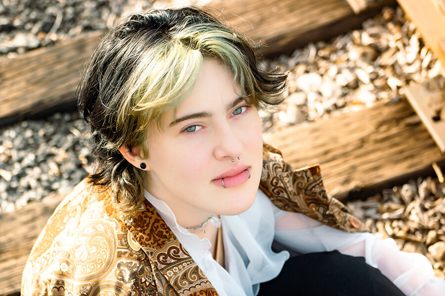 High school senior with many face piercings looking up while sitting on railroad tracks.