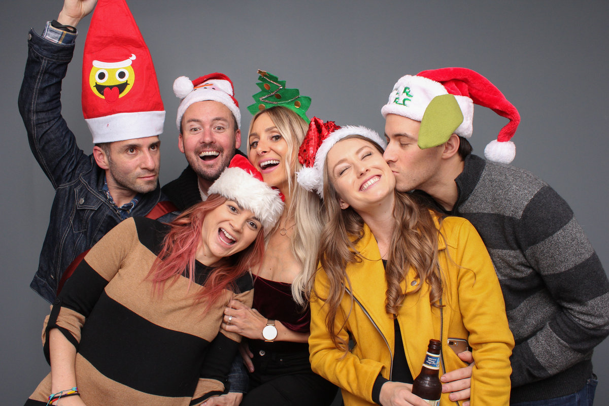 Group of friends snuggle up in a photo booth at a company Christmas party