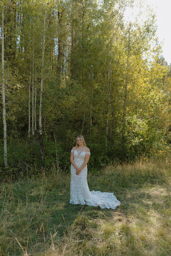 A portrait of a bride on her elopement day. She's in her wedding dress with lots of trees behind her.
