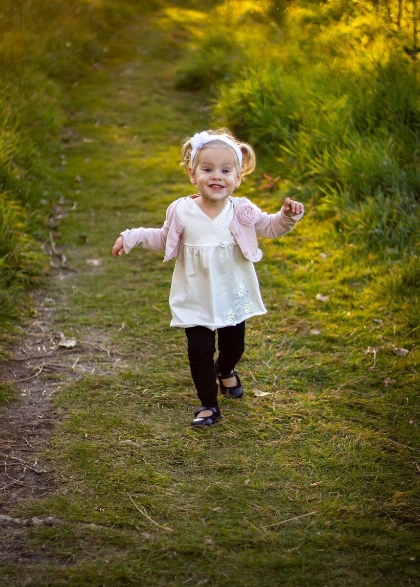 a toddler girl with pigtails runs in a field in Edmonton