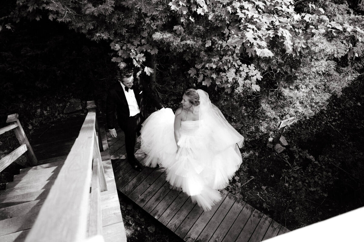 Black and white top-view photo of the bride and the groom walking on a wooden trail at The Ausable Club, New York.