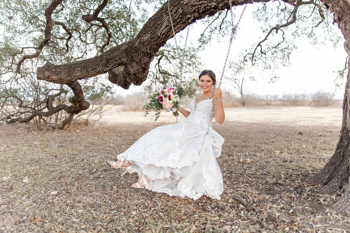 bride swings under large oak tree holding bouquet in San Antonio Texas