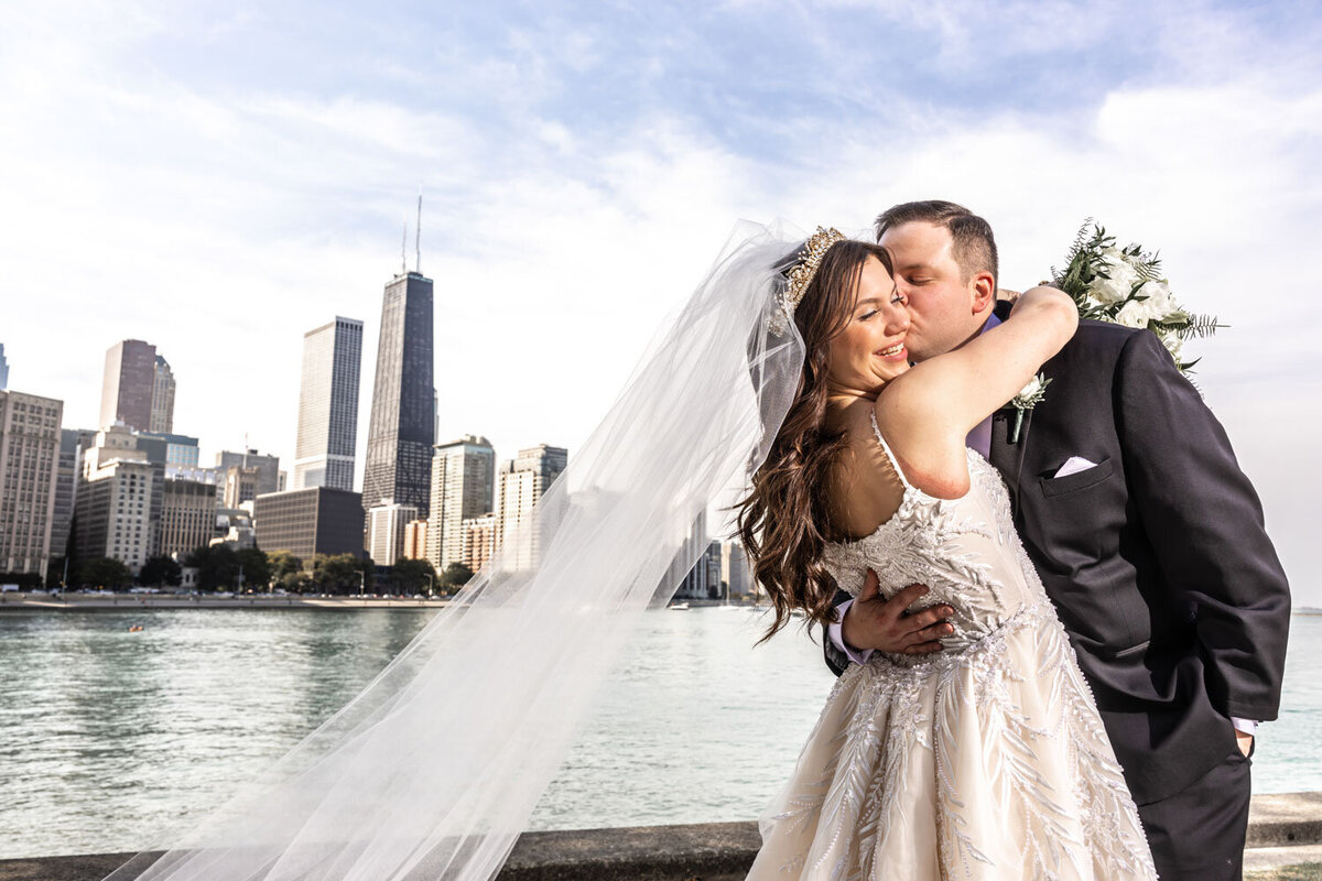 A bride and groom are kissing in front of a city skyline.