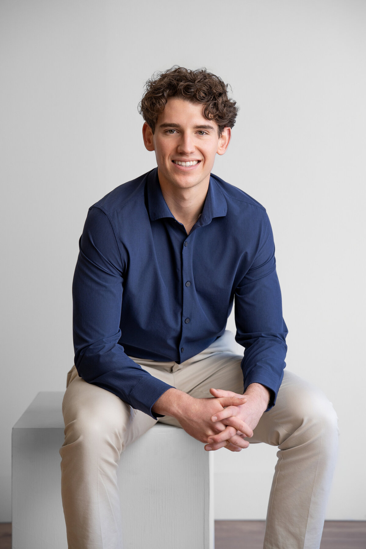 young man poses in a masculine way while smiling for his picture while wearing a button down