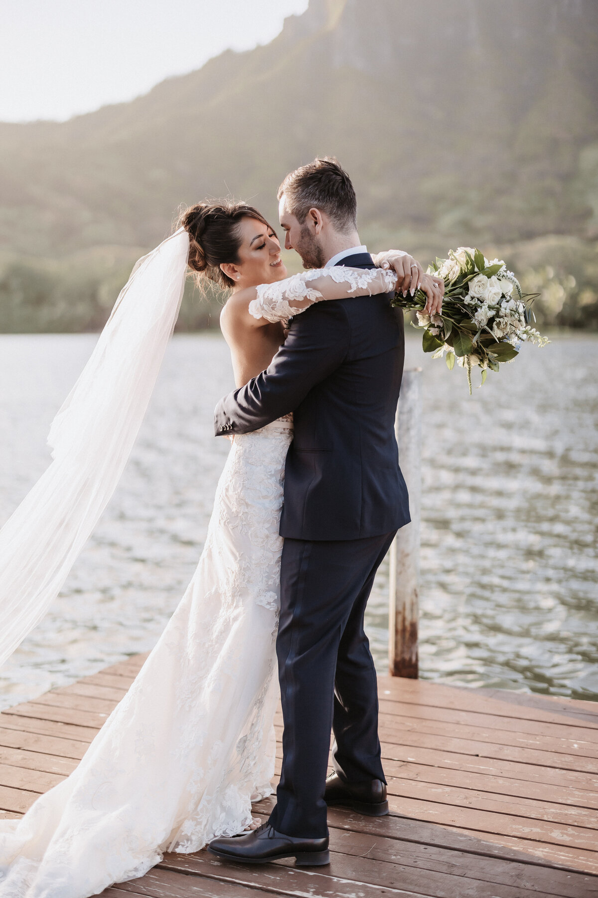 Wedding couple hugging holding wedding bouquet on dock at Kualoa Ranch