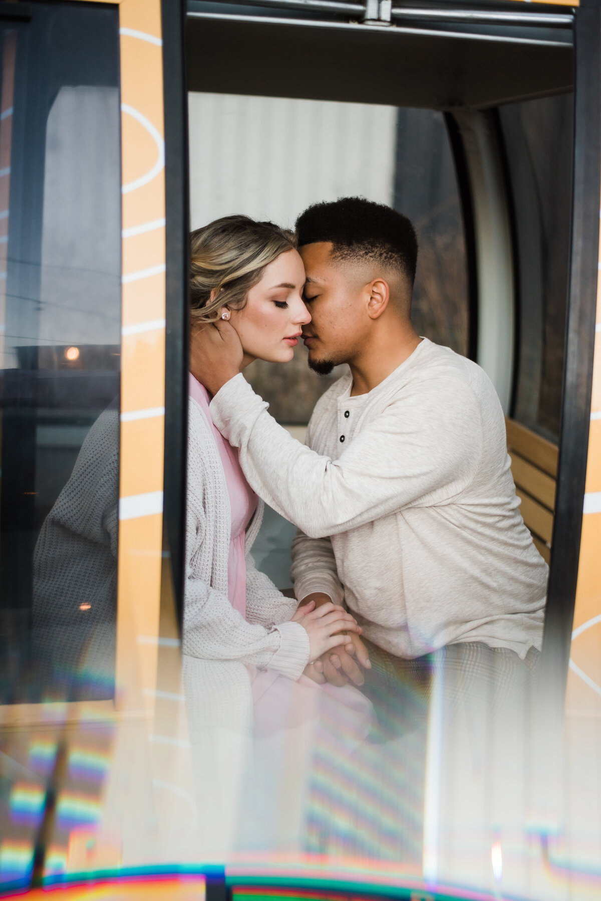 denver couples photography in downtown with man and woman sitting in a trolley cart as the man caresses the woman's jawline and leans in to whisper in her ear romantically captured by denver engagement photographer