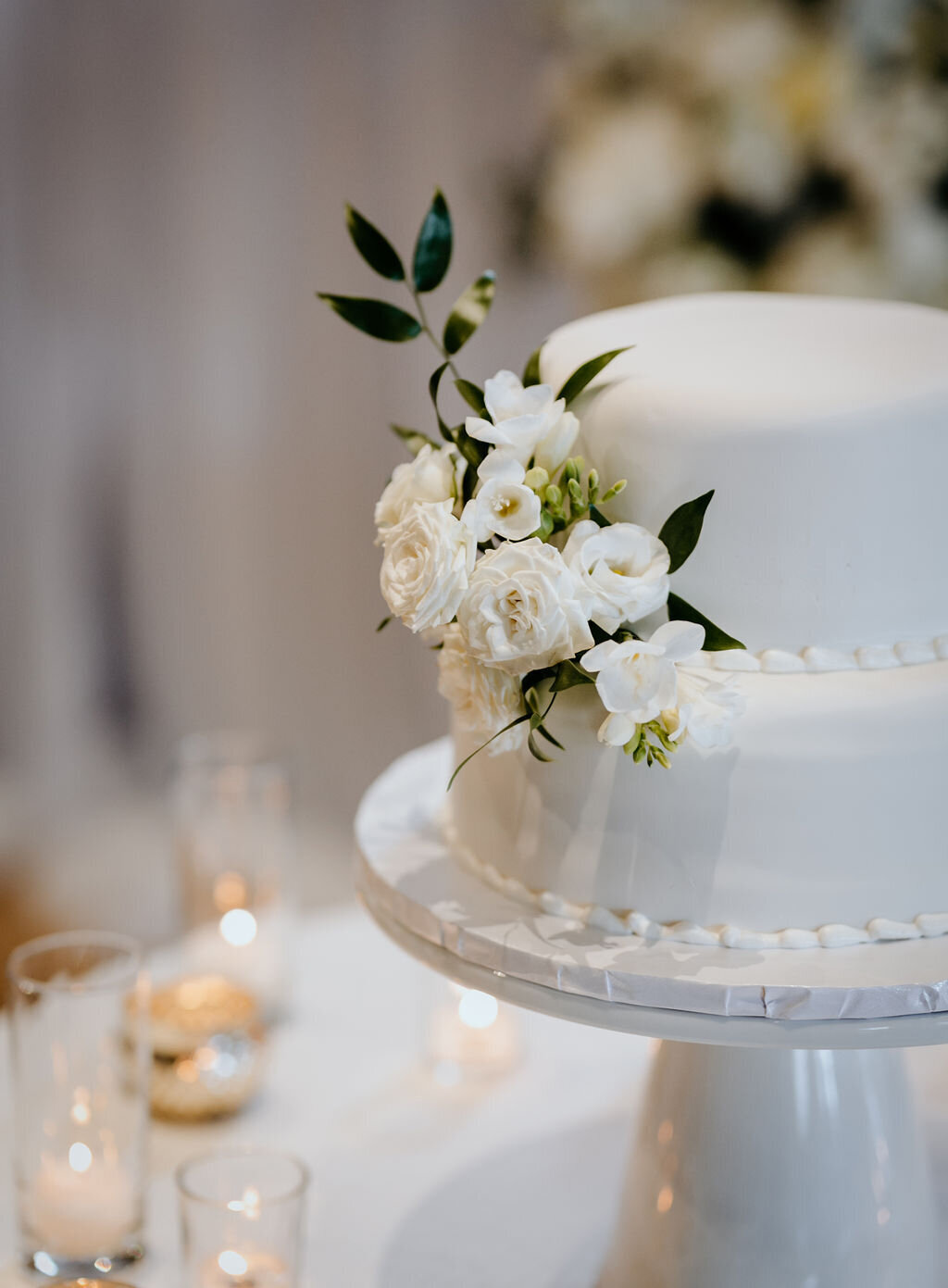 Close-up of a white two-tier wedding cake adorned with white flowers at a spring wedding at the Palm Event Center in Pleasanton, CA.