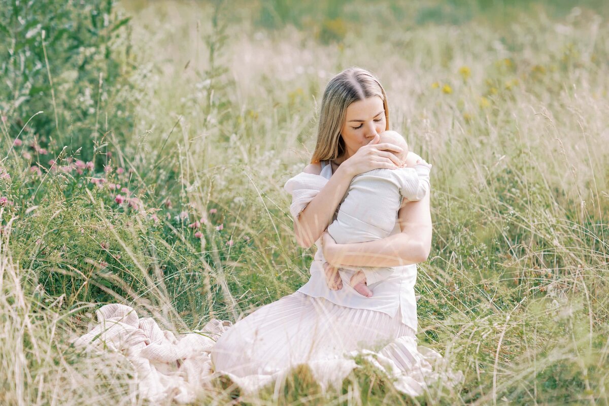 En mamma sitter i gräset och pussar sin bebis
