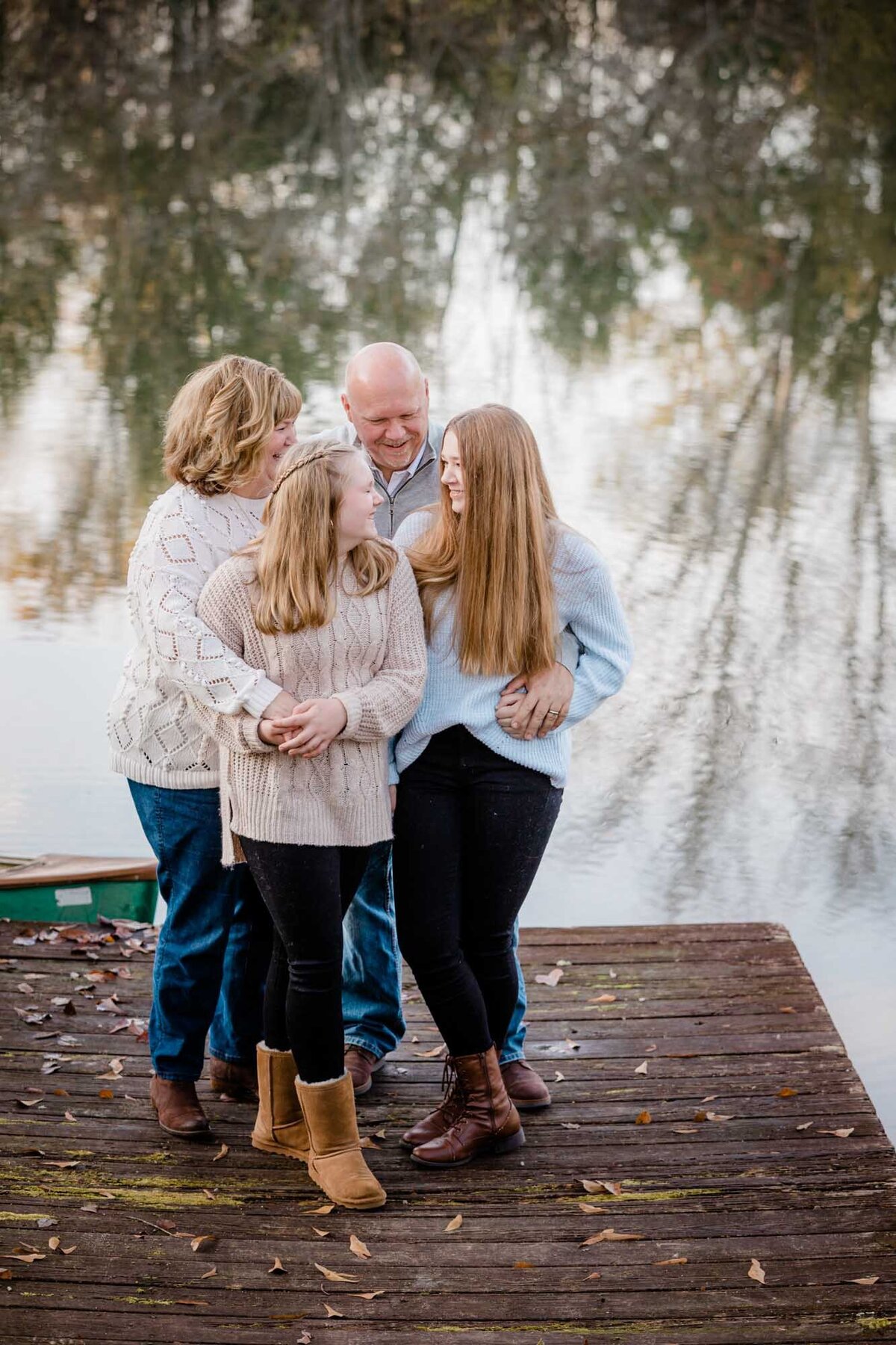 A family standing on a dock all huddled close together as they laugh and tell secrets during their session.