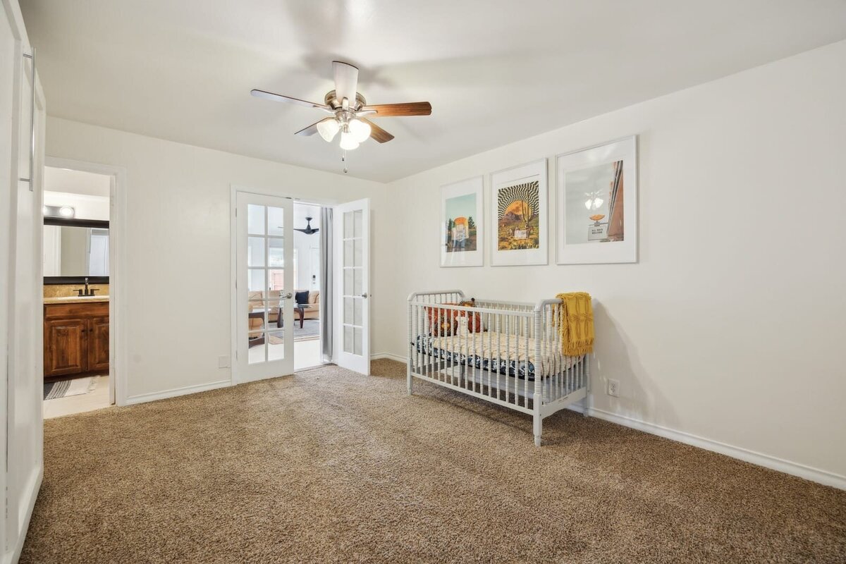 Bedroom at 3120 Chapel Downs Dr Dallas TX featuring nursery setup, carpeted floors, ceiling fan, and French doors to sunroom — listed by Haven Realty Group.