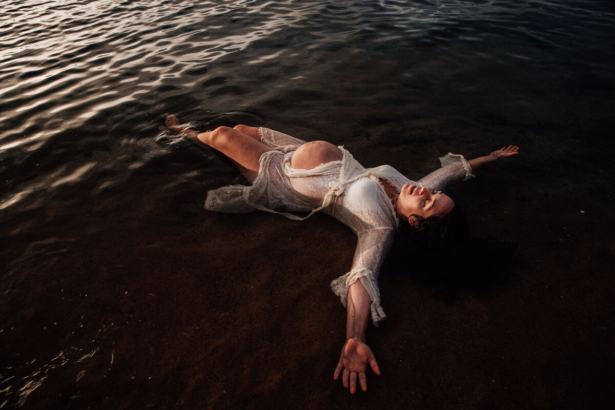 Pregnant woman lies belly up in water during melbourne beach photography session