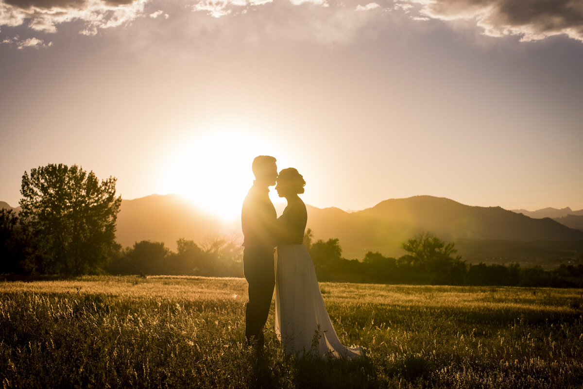 A silhouette of a groom kissing his bride on the forehead at golden hour.