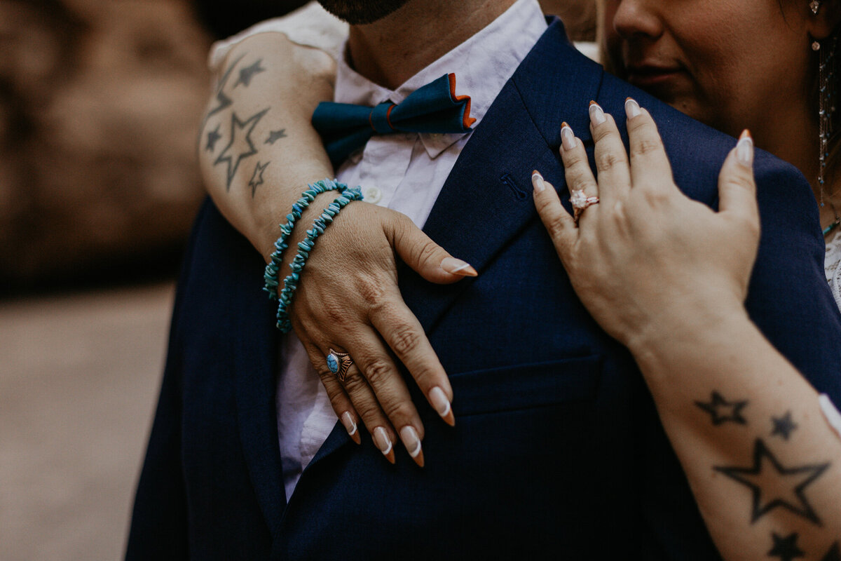 close up of brides hands and jewelry hugging her groom
