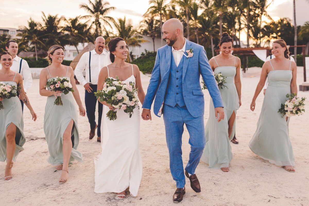 Bride, groom and bridal party walking on beach at wedding in Riviera Maya